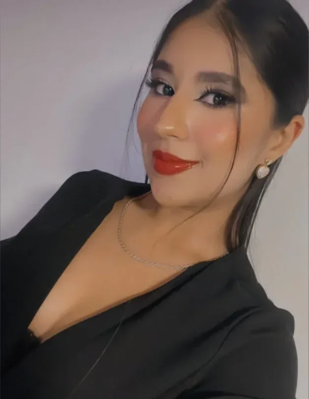 Maquillaje social con delineado alado, piel luminosa y labios rojos; cabello negro peinado hacia atrás y blusa negra.
