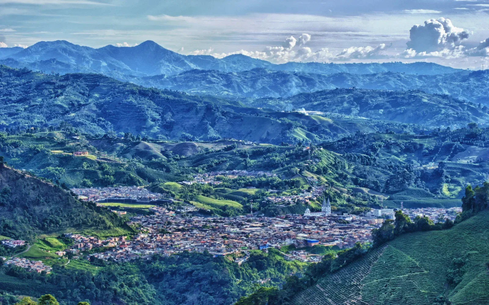 Paisaje de montañas cafeteras con un pueblo en el valle bajo un cielo con nubes.