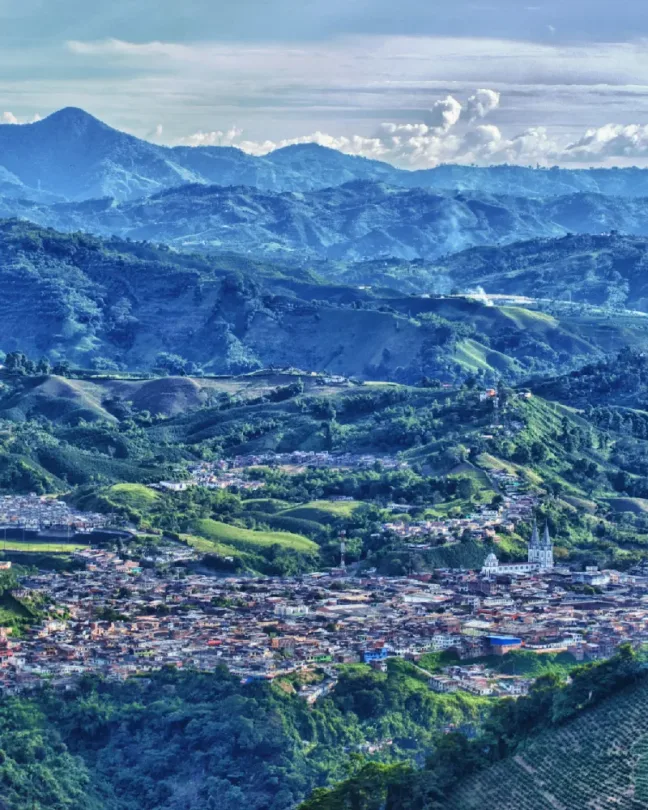 Paisaje de montañas cafeteras con un pueblo en el valle bajo un cielo con nubes.