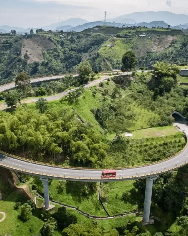 Viaducto curvo que atraviesa colinas verdes cubiertas de vegetación.