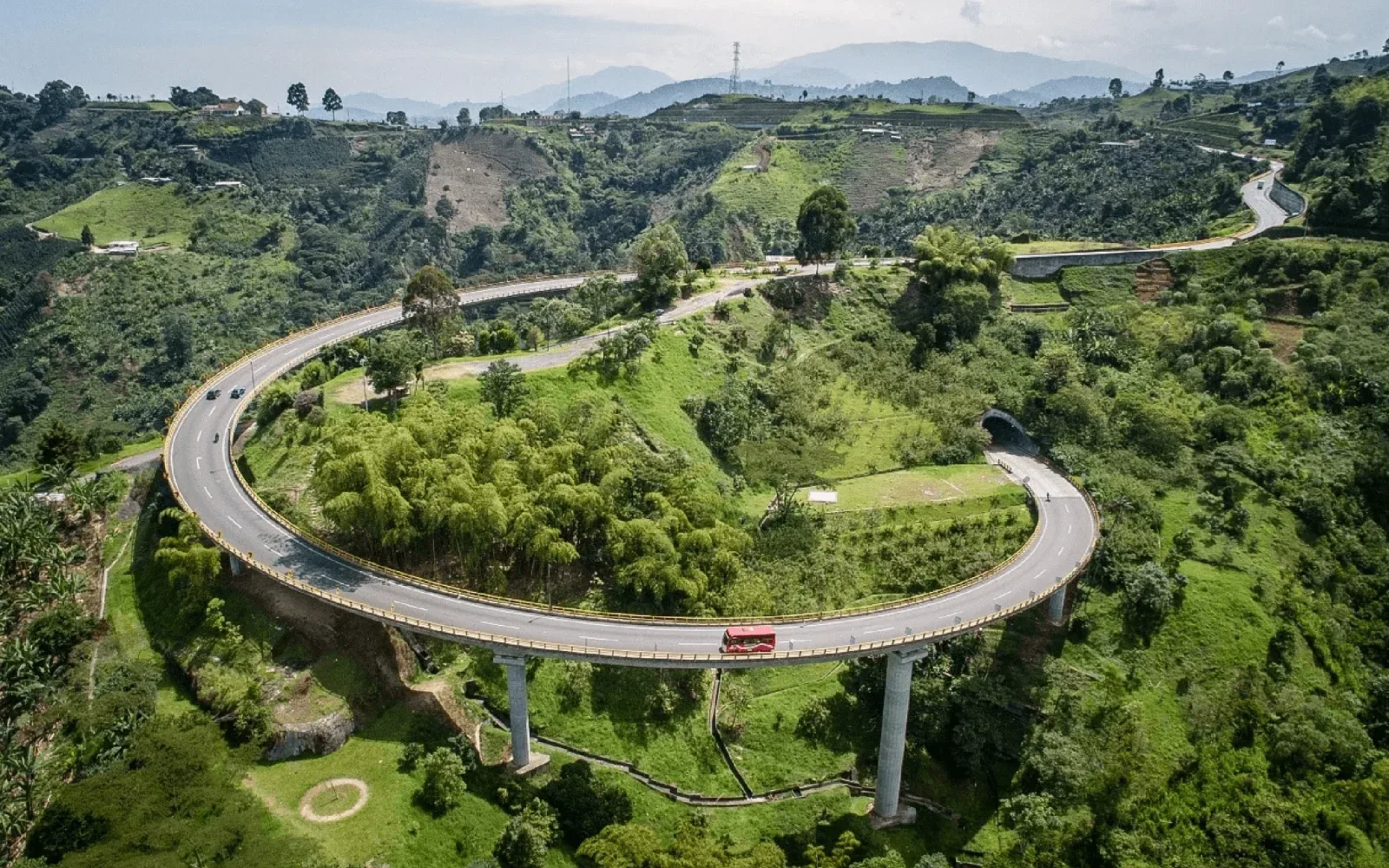 Viaducto curvo que atraviesa colinas verdes cubiertas de vegetación.