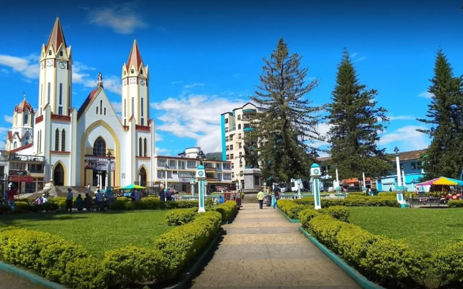 Iglesia de dos torres blancas frente a una plaza con jardines y senderos.
