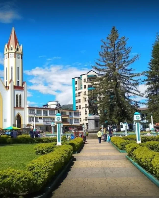 Iglesia de dos torres blancas frente a una plaza con jardines y senderos.