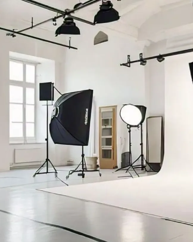 Estudio fotográfico blanco con una cámara en trípode, softboxes y luces de estudio.
