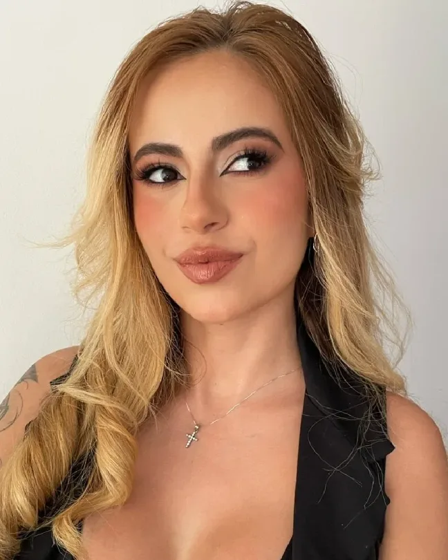 Maquillaje social glam con delineado alado, rubor rosado y labios nude brillantes; cabello rubio en ondas sueltas.