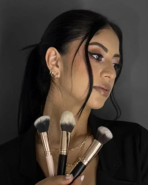 Retrato de Nille Cruz, maquilladora profesional, sosteniendo tres brochas de maquillaje.