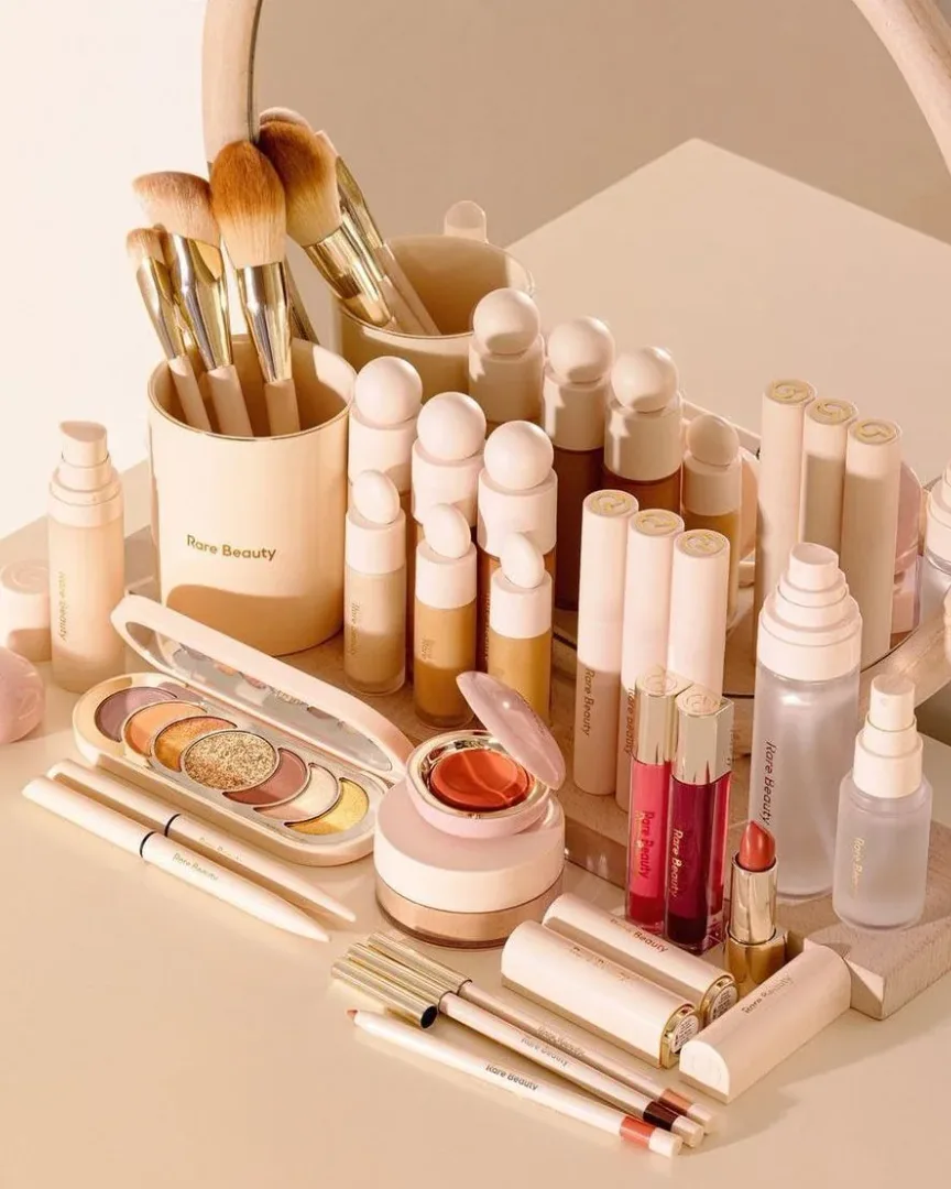 Brochas, sombras, labiales y otros cosméticos organizados frente a un espejo redondo.