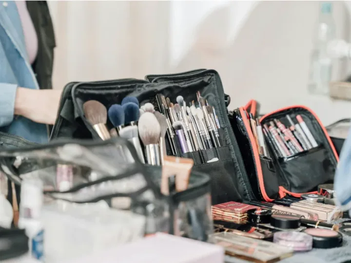 Maletín abierto con brochas, pinceles y paletas de maquillaje sobre una mesa.