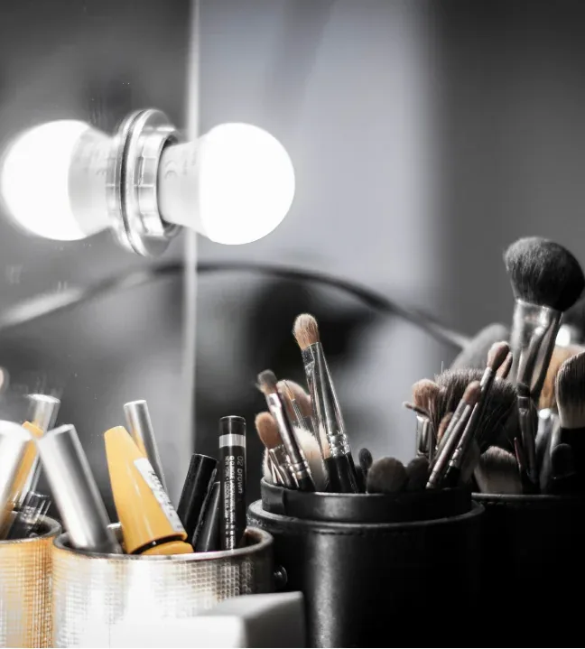 Brochas y productos de maquillaje organizados frente a un espejo iluminado.