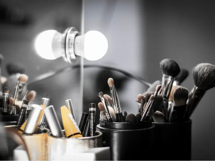 Brochas y productos de maquillaje organizados frente a un espejo iluminado.