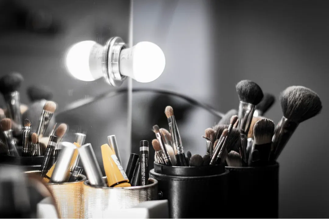 Brochas y productos de maquillaje organizados frente a un espejo iluminado.